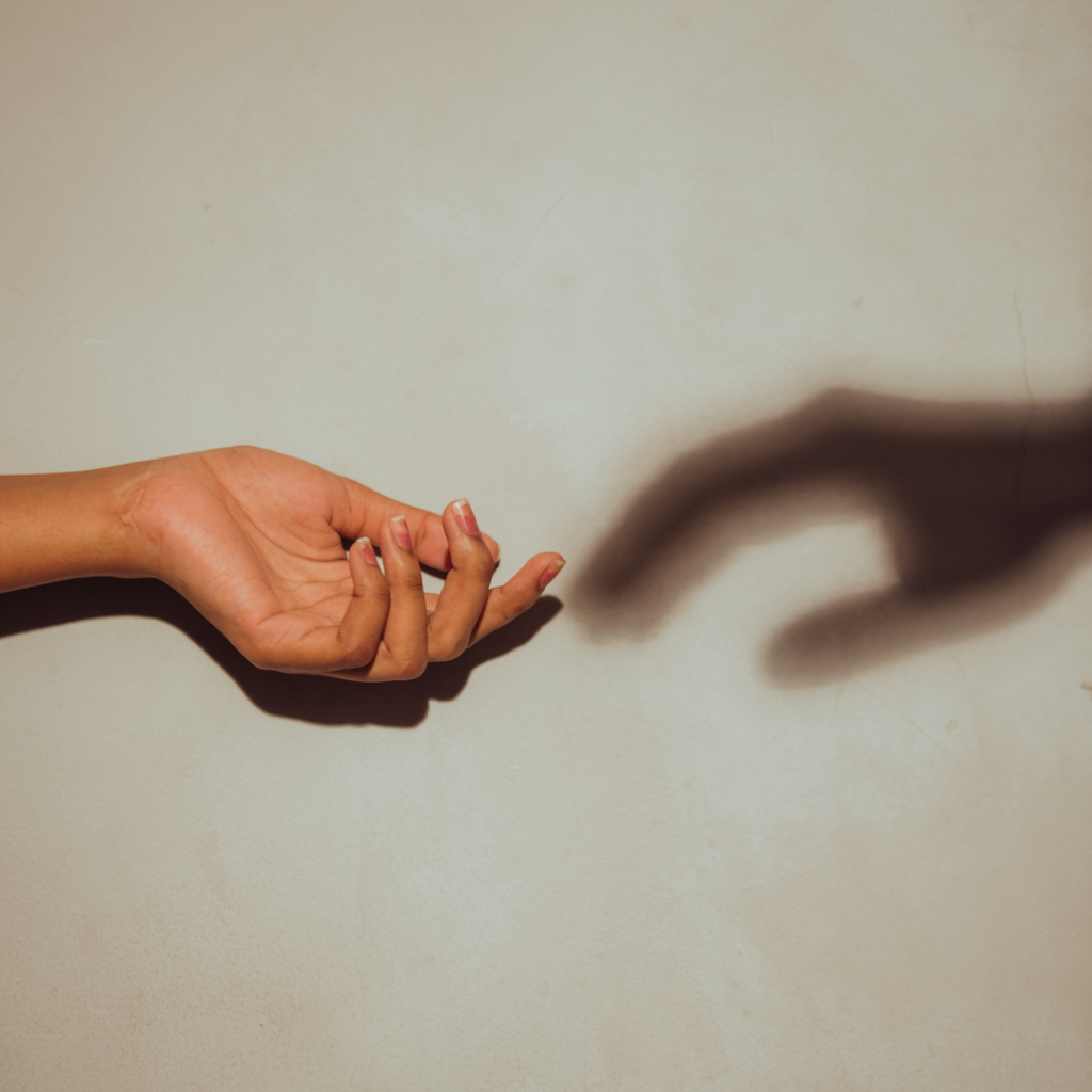 Image of a hand reaching out and being met by its own shadow 