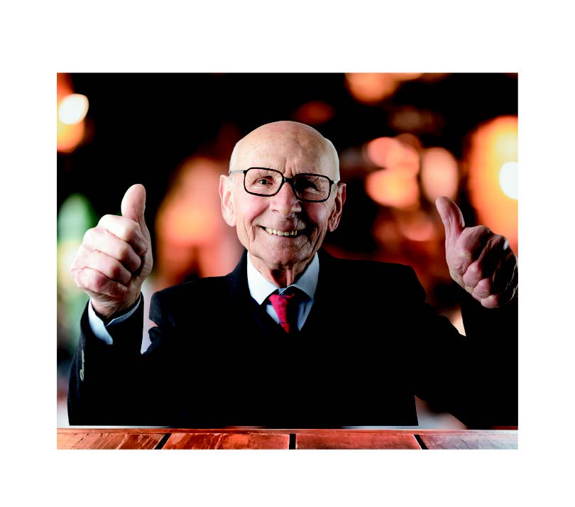 Image of an older male sitting behind a table smiling with his thumbs up