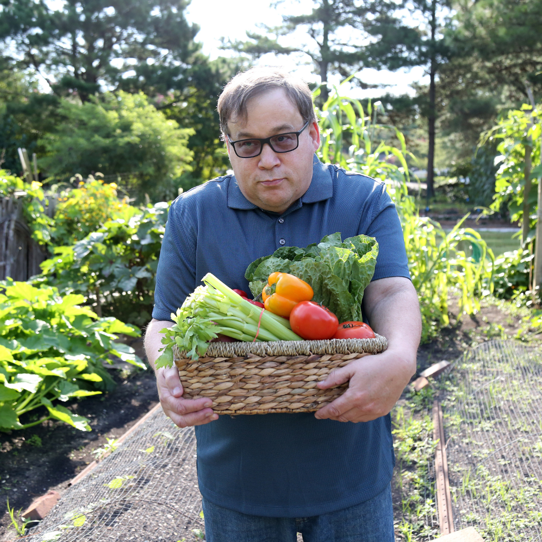 Image of man in a garden holding a basket of vegetables.