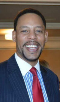 Photo of male, smiling and wearing a red tie and blue pinstriped suit.