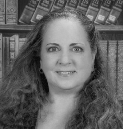 Black and white photo of a woman with long curly hair, smiling in front of a bookcase