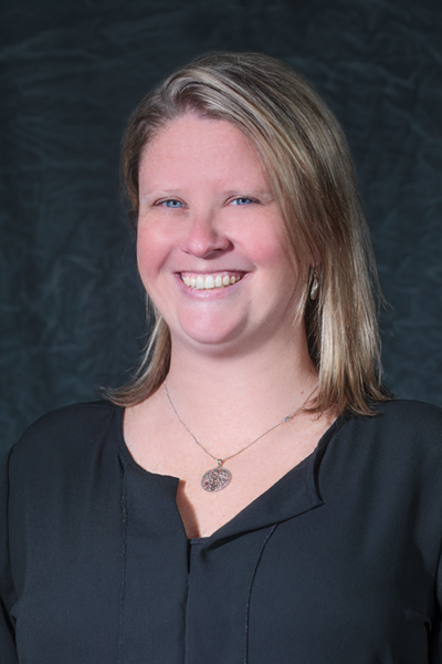 Gray Background. Professional headshot of female smiling, with short blonde hair and a black shirt