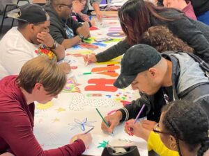 Group of staff and Day Habilitation program consumers decorating a thank you banner for people who support the program.