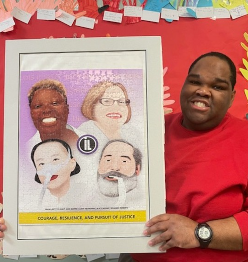 Image of a male consumer wearing a red sweater, holding a framed puzzle that he put together himself.